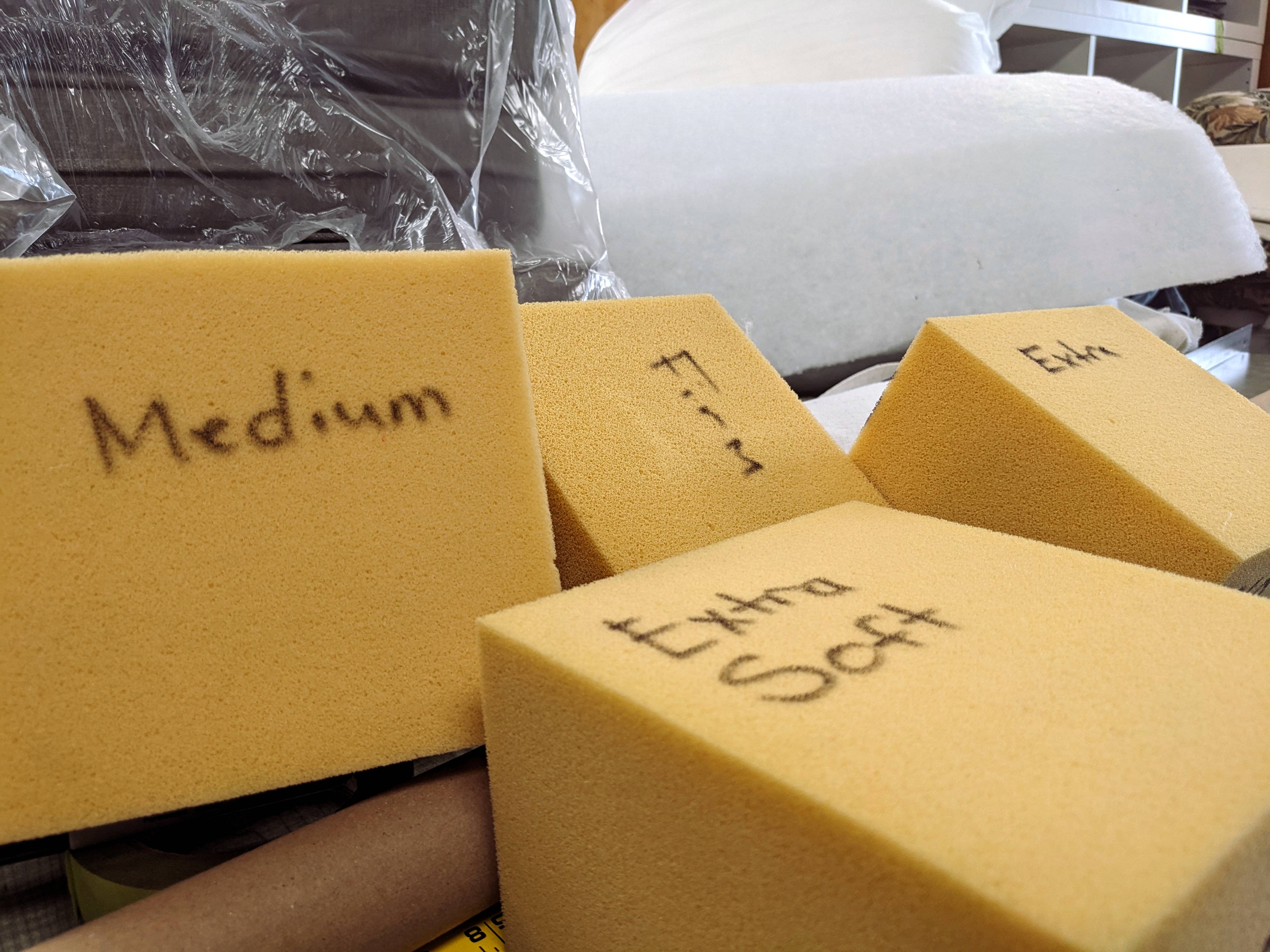 Gold polyurethane foam blocks hand-labelled Medium, Extra Soft, and Extra at an upholstery shop, with white Dacron wrap visible in the background