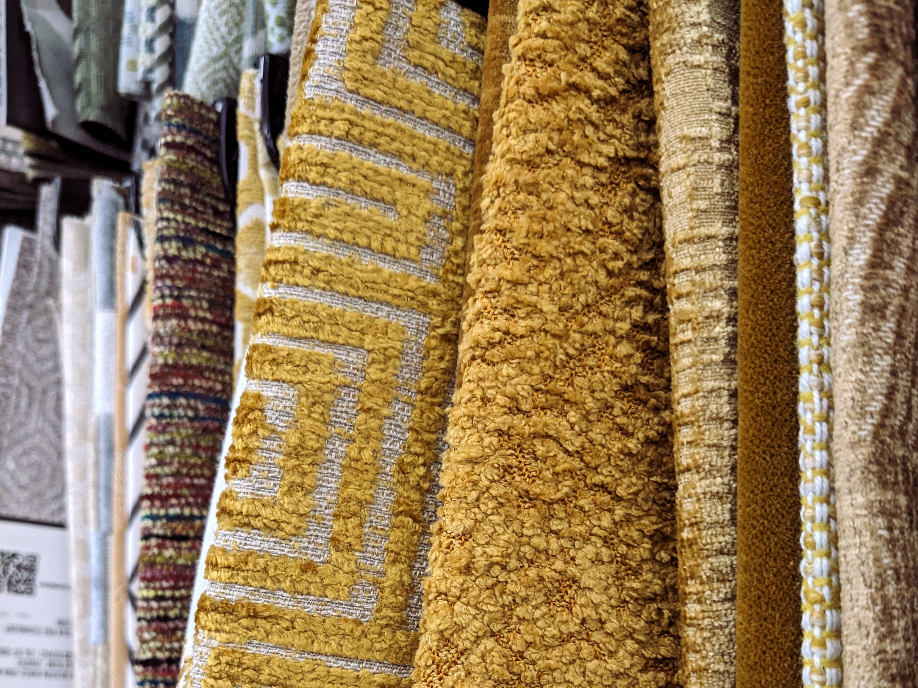 Rolls of upholstery fabric in gold chenille and woven textural patterns hanging in a trade fabric showroom